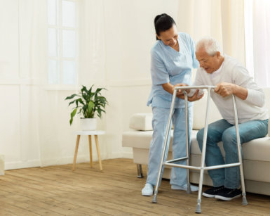 caregiver assisting a senior man to stand up using her walking frame