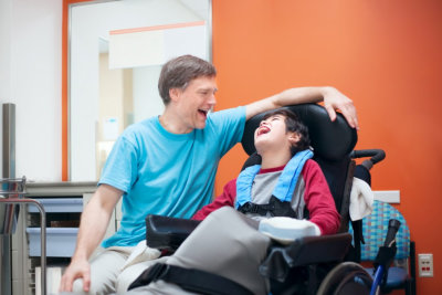 adult man talking with the little boy sitting in wheelchair smiling