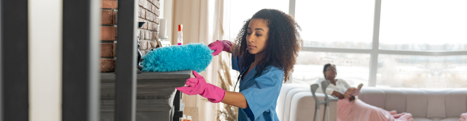 caregiver wearing pink gloves dusting the fireplace in the living room