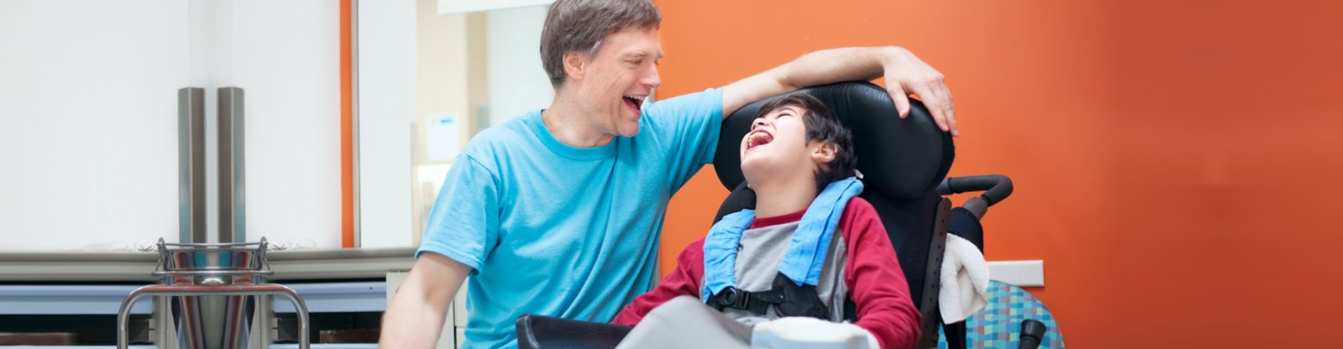 adult man talking with the little boy sitting in wheelchair smiling